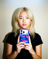 A woman with bleached hair is holding a phone with a phone case that has swirls of blue and pink and rounded edges
