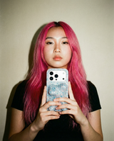 A woman with pink hair is holding a phone with a phone case that is speckled blue, pink and white with a sculptural shape