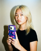 A woman with bleached hair is holding a colorful phone case with a sculptural shape