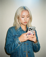 Person wearing a denim jacket holding a phone with a clear magsafe grip with flowers in a light background
