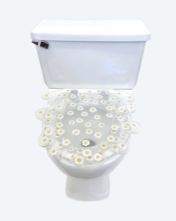 White toilet with clear lid with white flowers suspended in the toilet seat